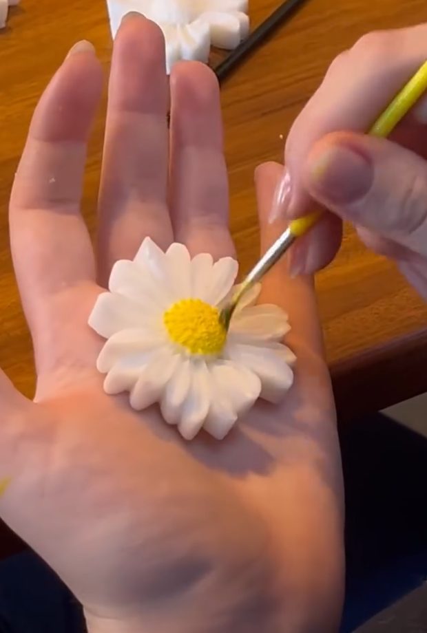 Mão segurando um sabonete em forma de margarida enquanto o miolo é pintado com pincel